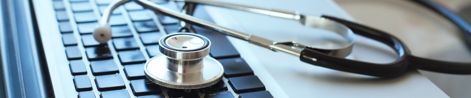 Hands typing on laptop with stethoscope representing medical coding and charge capture